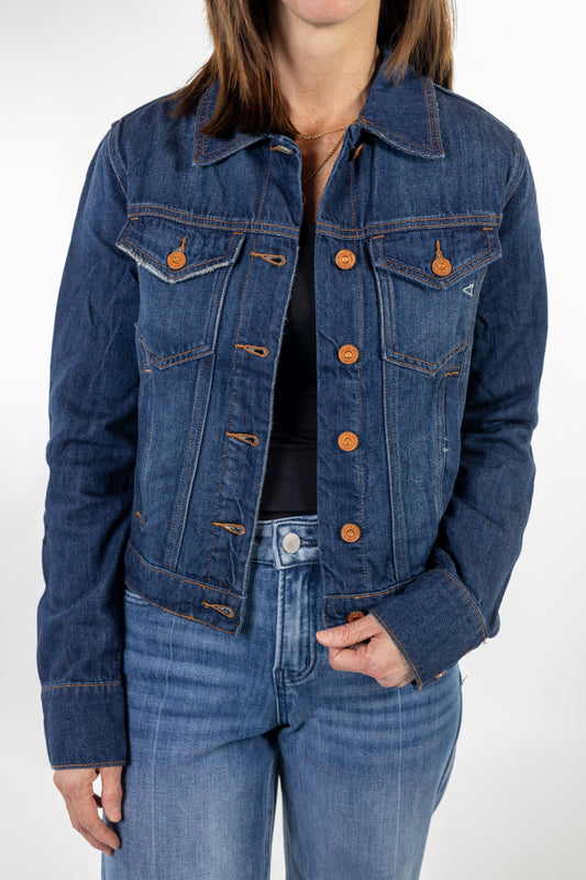 A woman wearing a cropped dark blue denim jacket with copper buttons, styled with blue jeans and a black top, shown from the neck down against a light gray studio background.