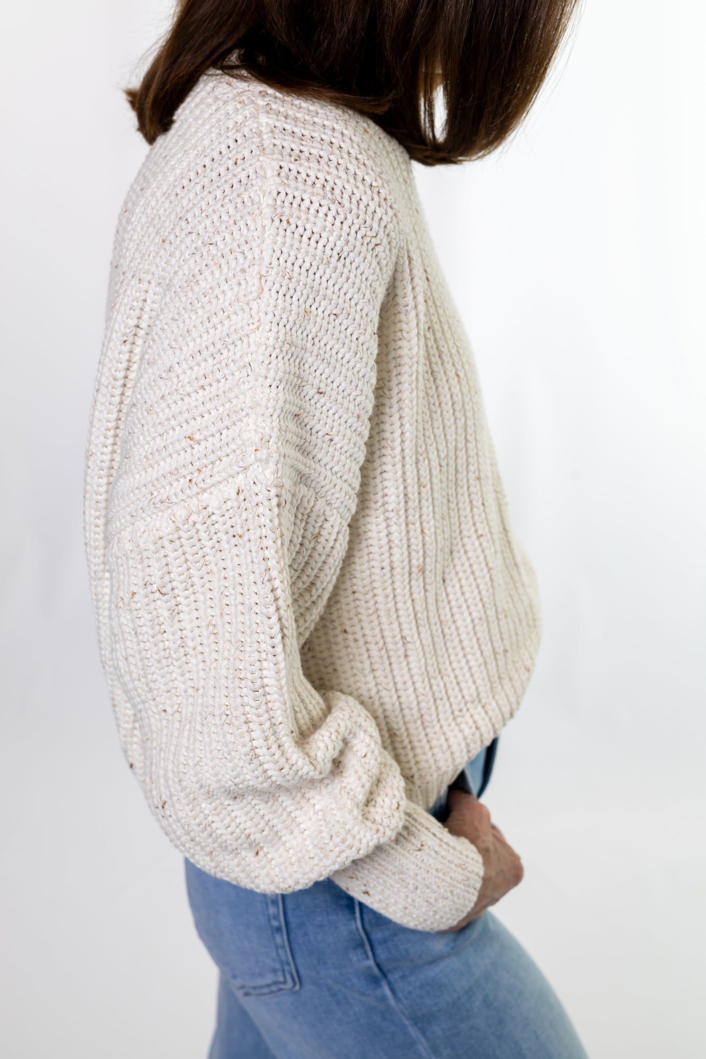 Person wearing a cream knitted sweater and blue jeans on a white background