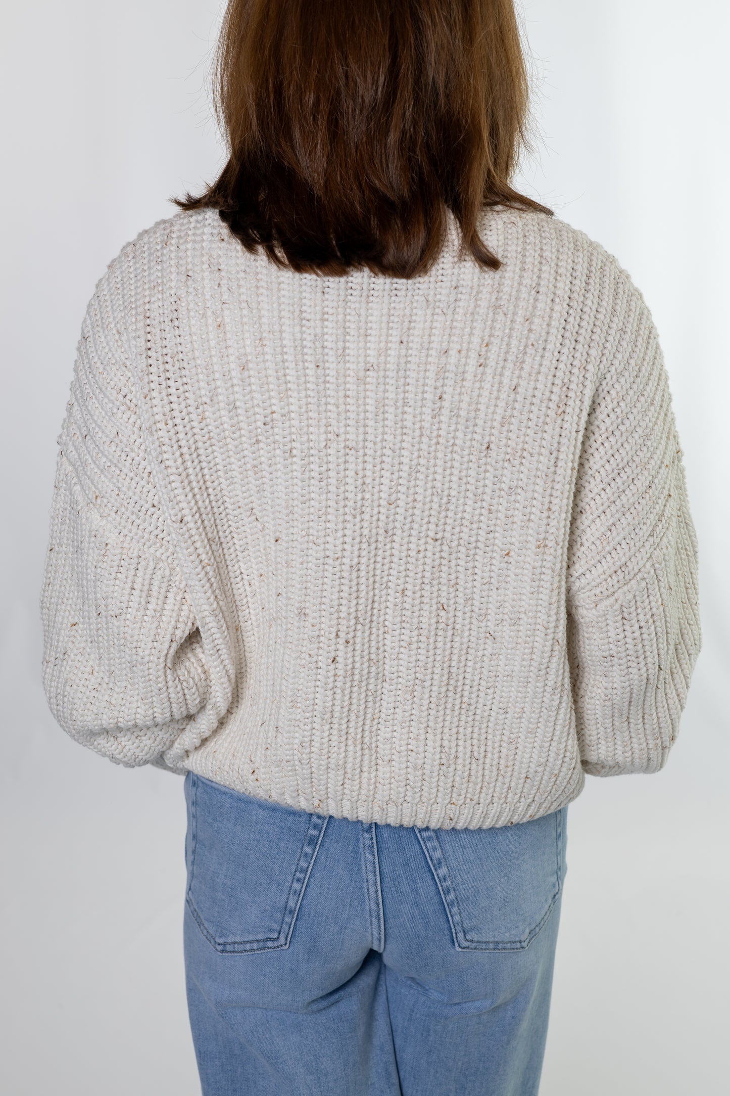 Person wearing a chunky knit sweater and blue jeans on a white background