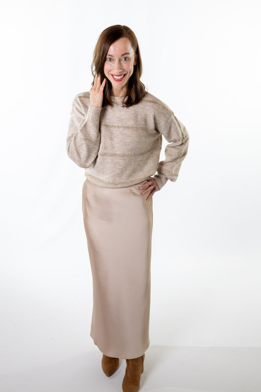 Woman wearing a beige sweater and champagne skirt on a white background