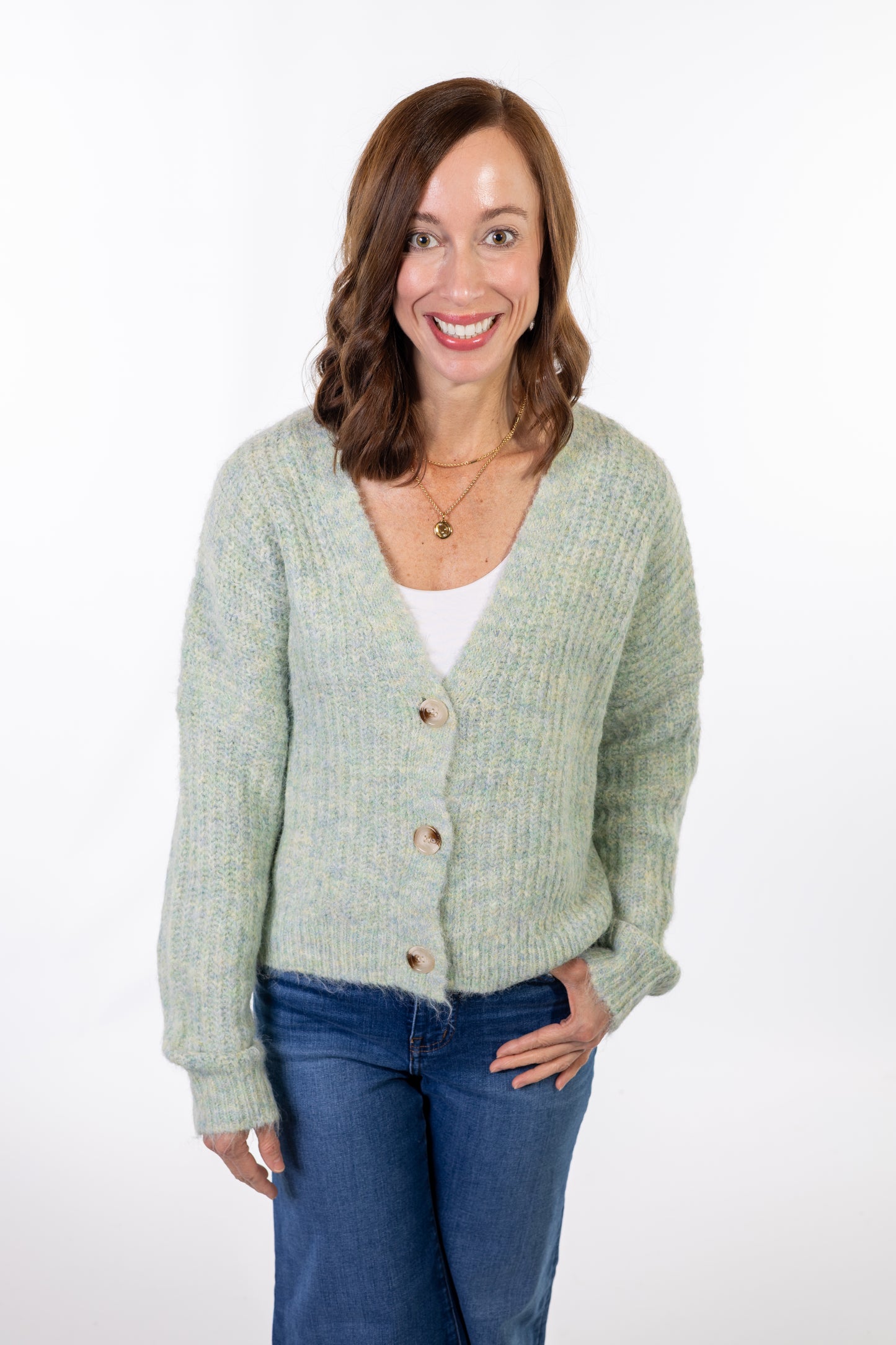 Woman wearing a light green cardigan over a white shirt with blue jeans on a white background