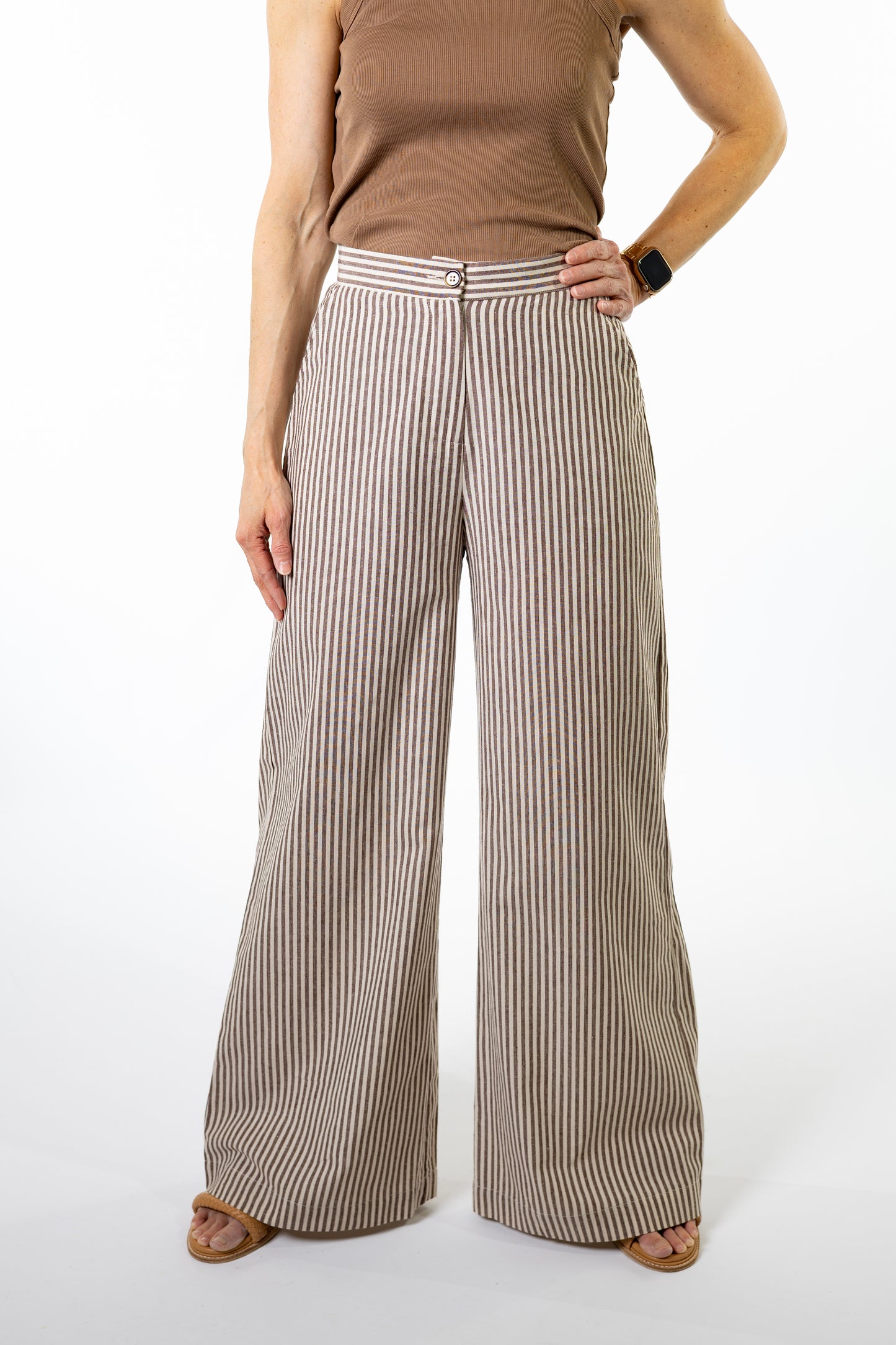 Woman wearing a brown tank top and brown and white wide-leg striped pants on a white background