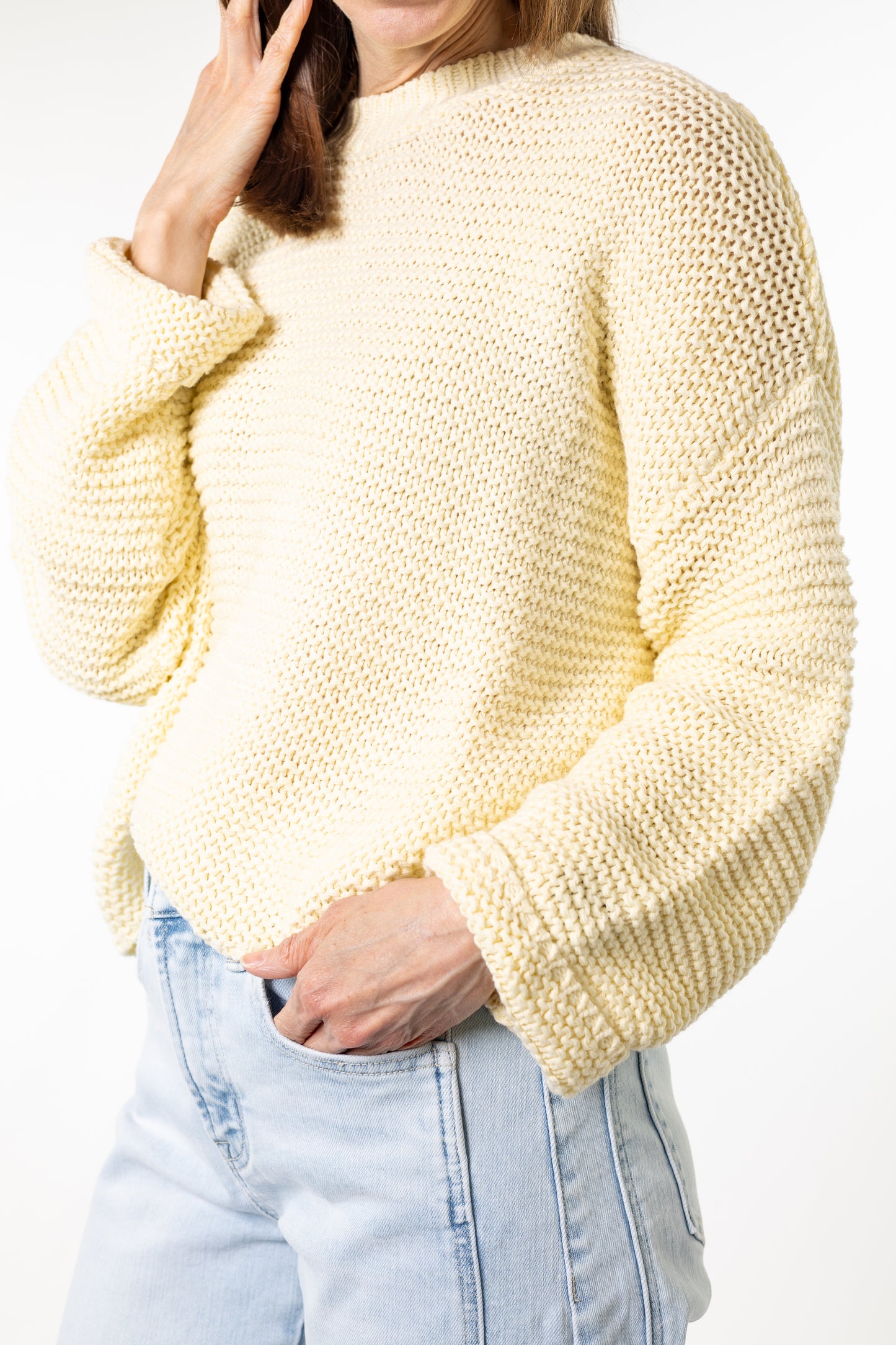 Person wearing a light yellow knitted sweater and light blue jeans on a white background
