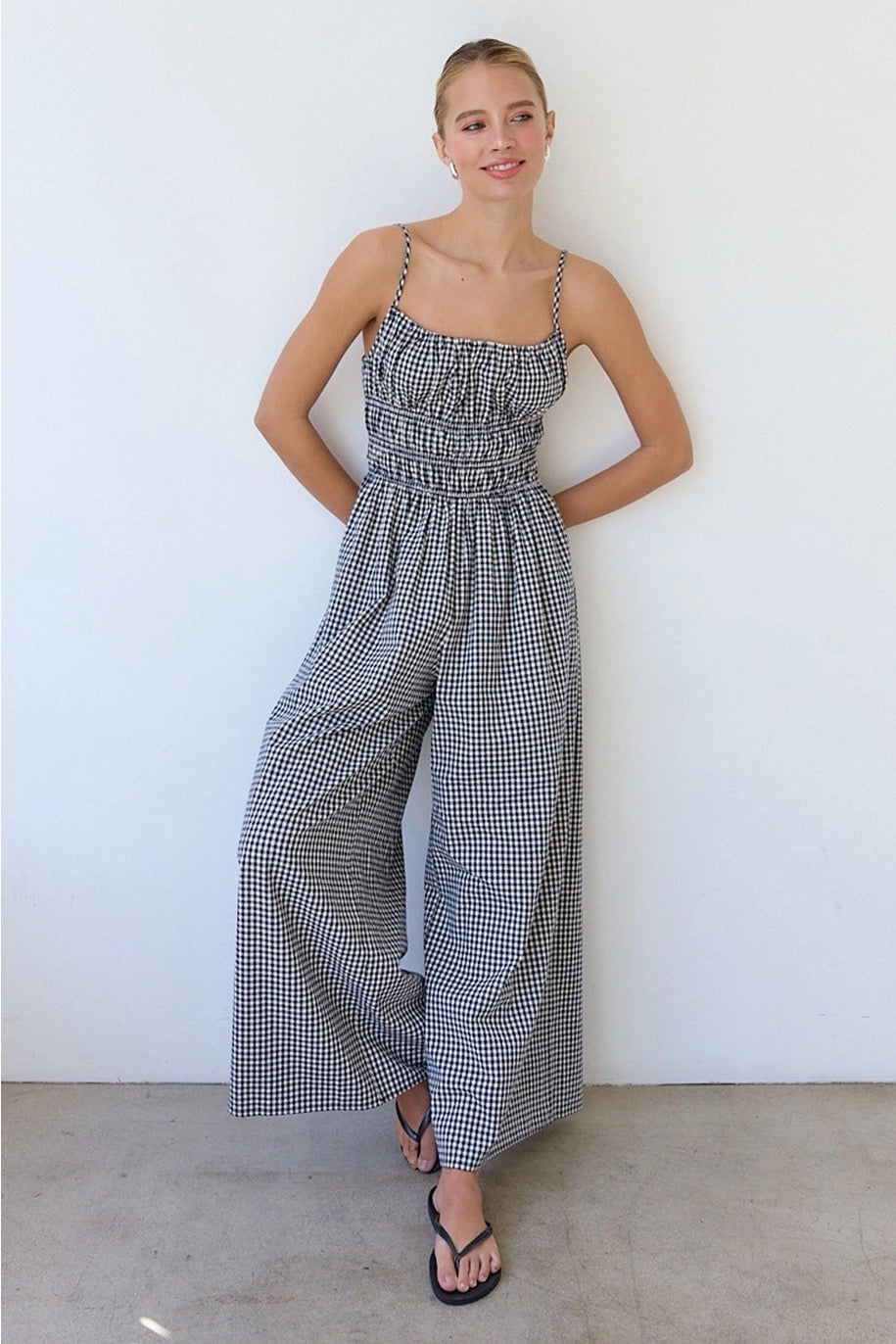 Woman wearing a navy and white checkered jumpsuit against a white wall.