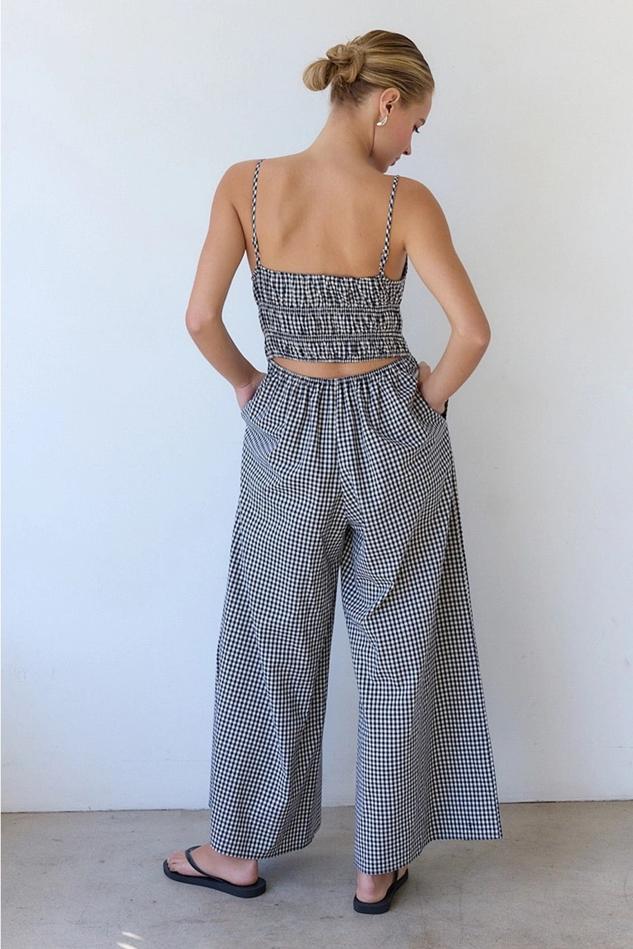 Woman wearing a checkered top and wide-leg pants against a white wall.