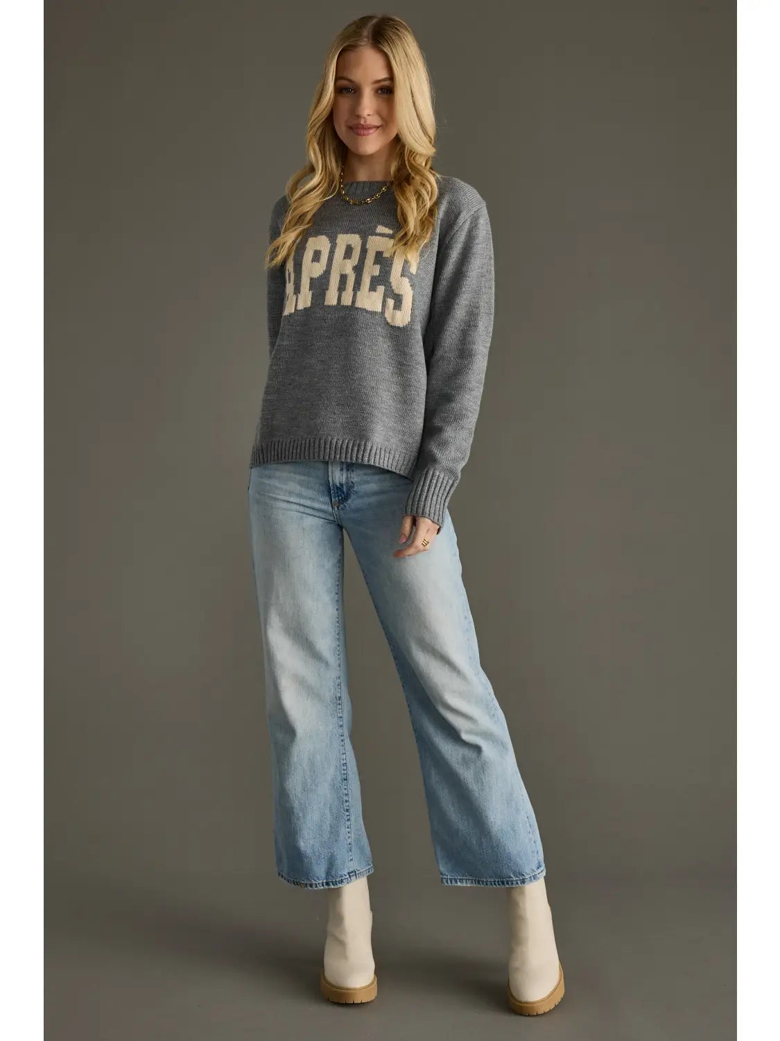 Woman wearing a gray sweater with 'APRES' text and blue jeans on a gray background