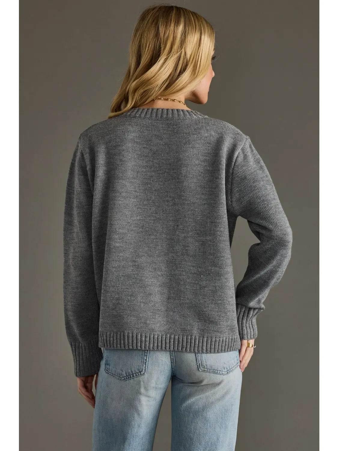 Person wearing a gray sweater and blue jeans against a plain background