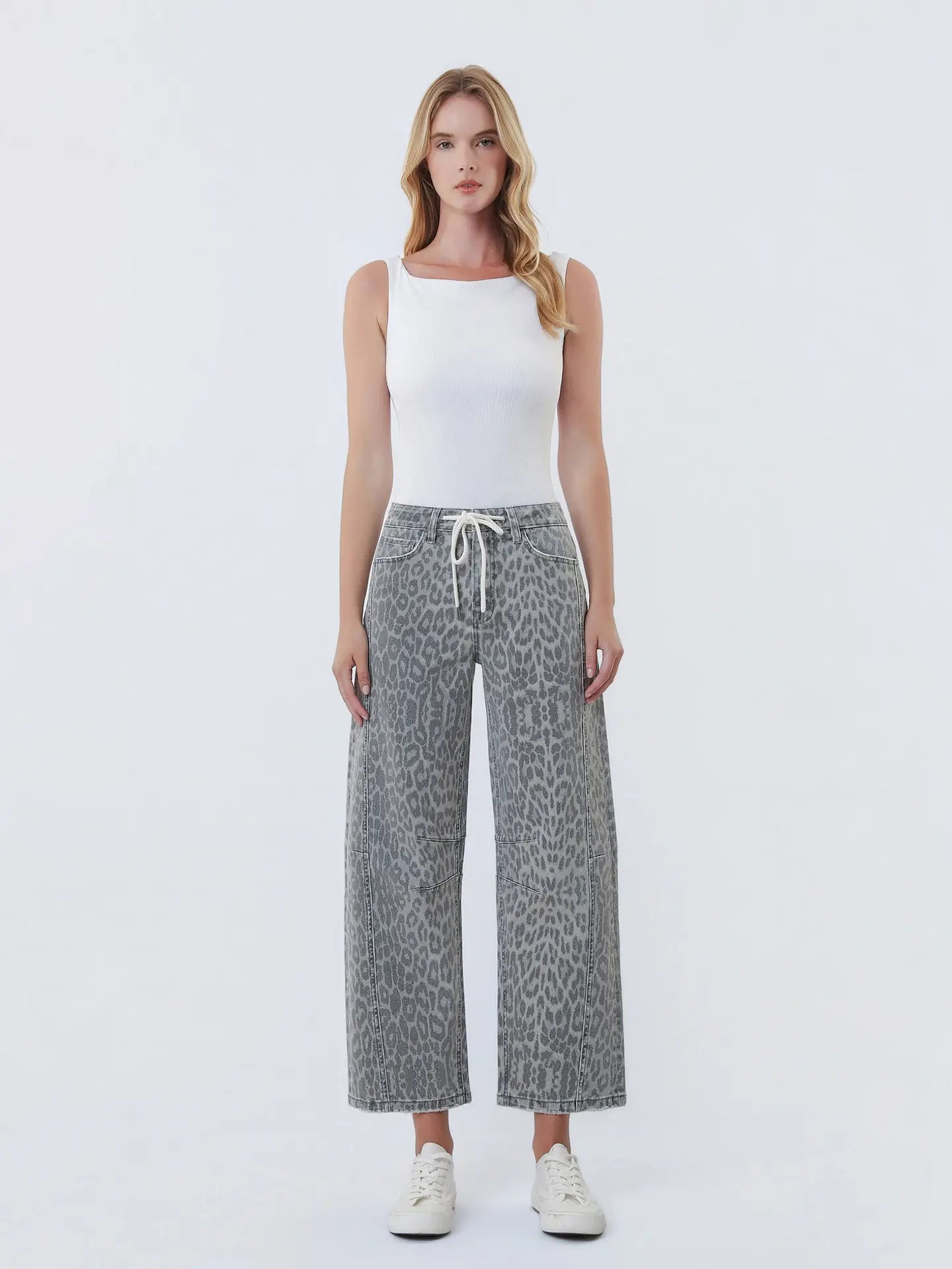 Woman wearing a white tank top and gray leopard print pants on a white background