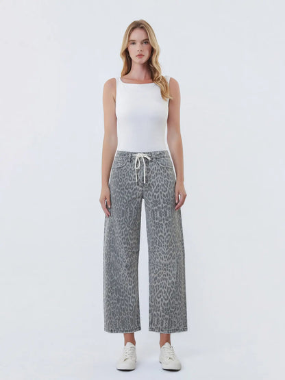 Woman wearing a white tank top and gray leopard print pants on a white background