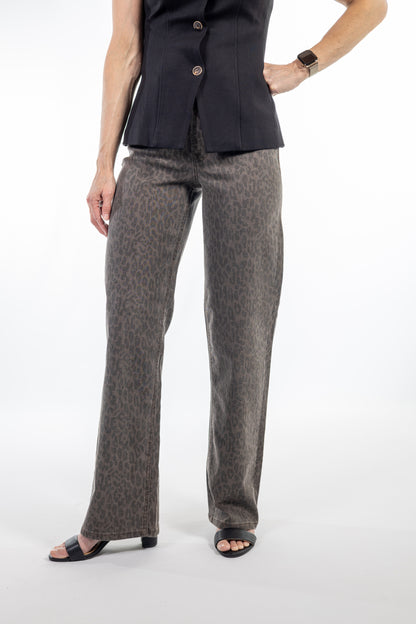 A model wearing a pair of wide-leg trousers in a brown and gray leopard print, paired with a black peplum top and black slide sandals, against a plain white studio background.