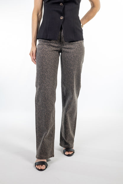 A model wearing a pair of wide-leg trousers with a brown and gray leopard print pattern, styled with a black sleeveless top and black slide sandals against a white studio background.