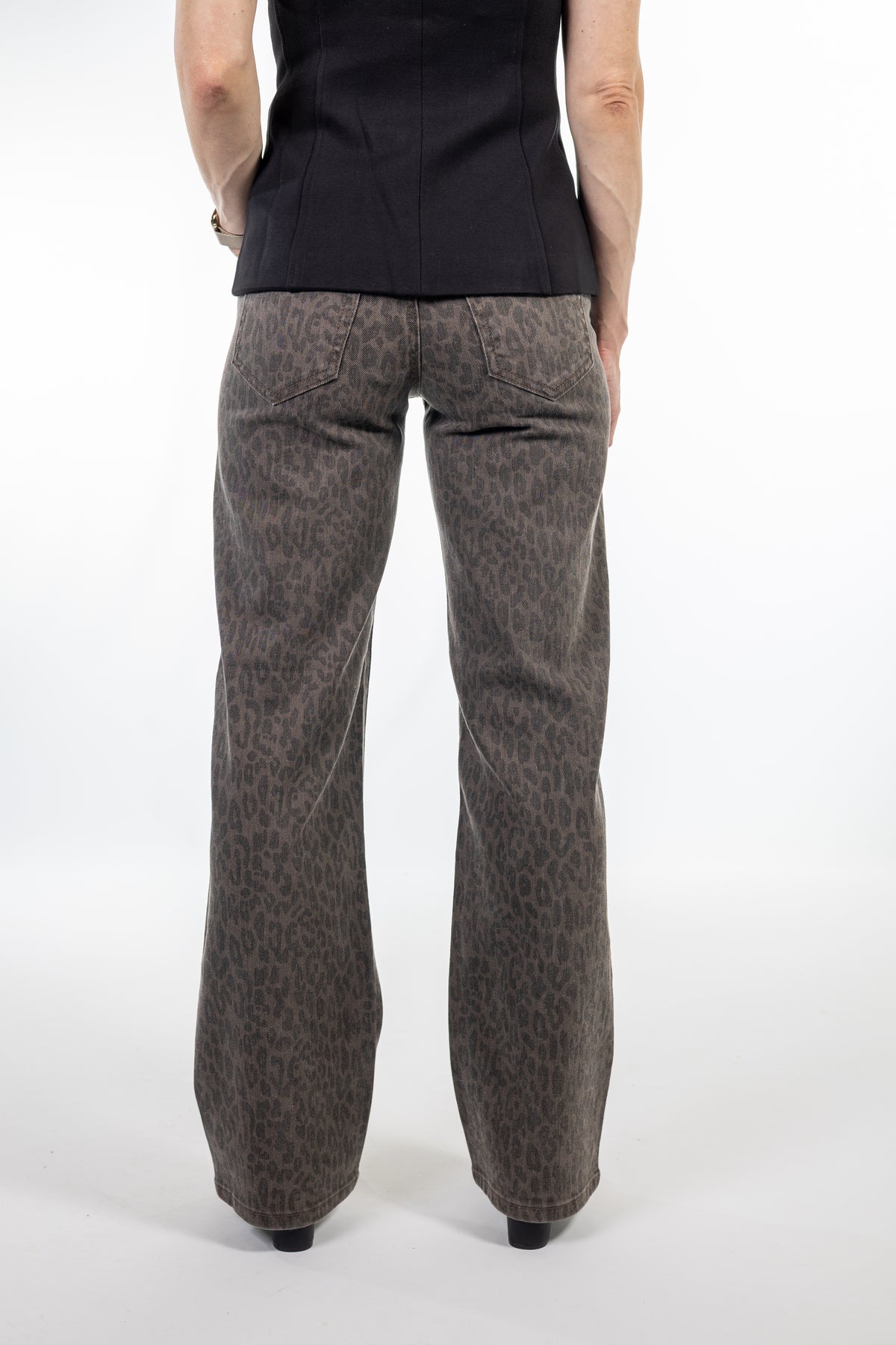 A person shown from the back wearing wide-leg brown pants with a subtle leopard print pattern, paired with a black top, against a plain white studio background.