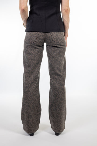 A person shown from the back wearing wide-leg brown pants with a subtle leopard print pattern, paired with a black top, against a plain white studio background.