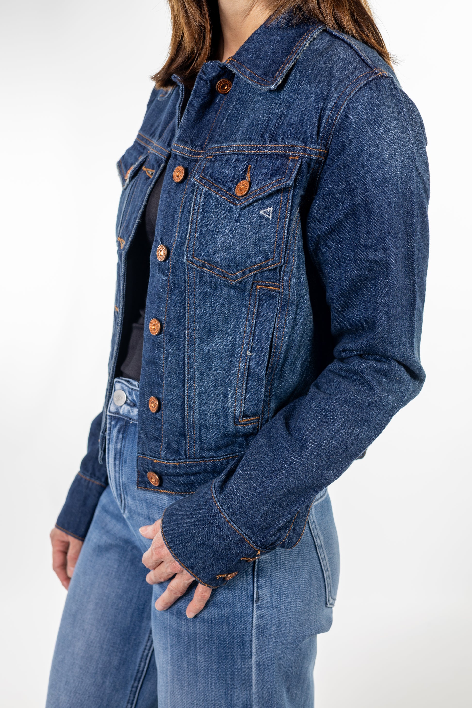 A close-up of a person wearing a cropped blue denim jacket with copper-toned buttons over a black top and blue jeans.