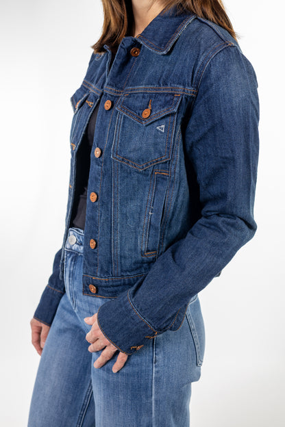 A close-up of a person wearing a cropped blue denim jacket with copper-toned buttons over a black top and blue jeans.