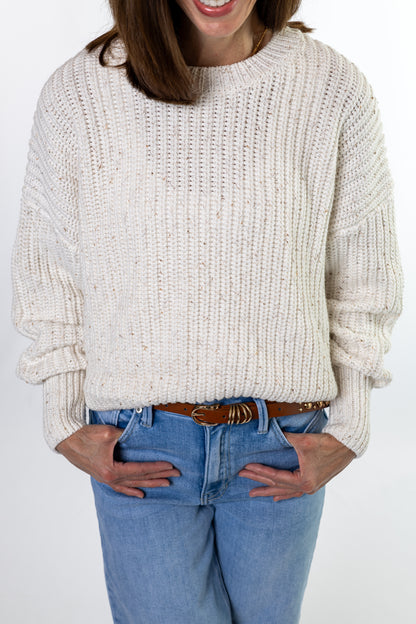 Person wearing a cream knitted sweater and blue jeans on a white background