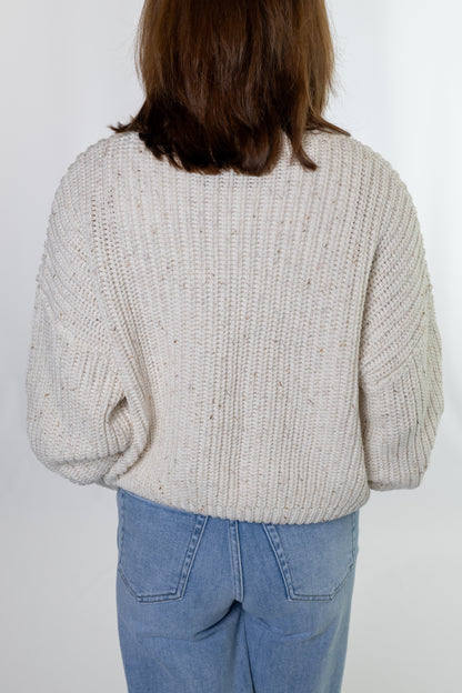 Person wearing a chunky knit sweater and blue jeans on a white background