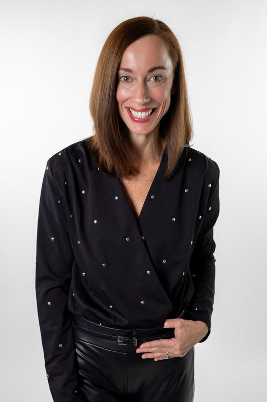 Woman wearing a black studded wrap bodysuit from Salt & Lavender Clothing, styled with faux-leather pants and jeans — chic holiday outfit for a night out or seasonal event in Dublin and Powell, Ohio.