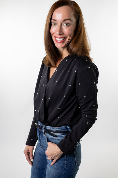 Black wrap bodysuit detailed with silver studs, styled with jeans and sleek faux-leather — sophisticated night-out and holiday look from Salt & Lavender Clothing, boutique apparel in Dublin, Ohio.