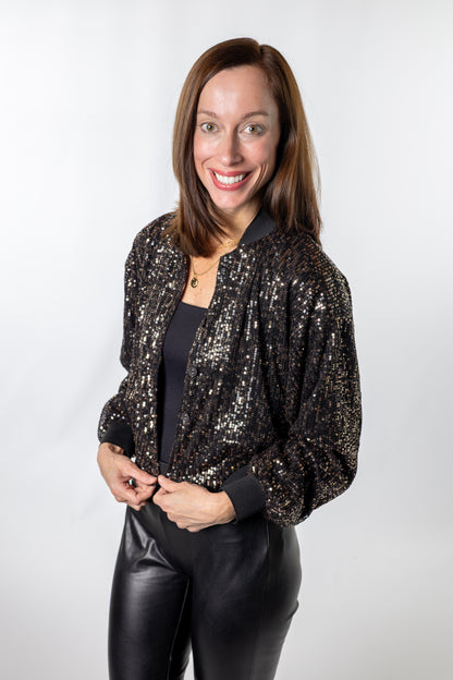Black and gold sequin bomber jacket styled with a black top and faux-leather pants — easy, elevated outfit for holiday dinners or date nights.