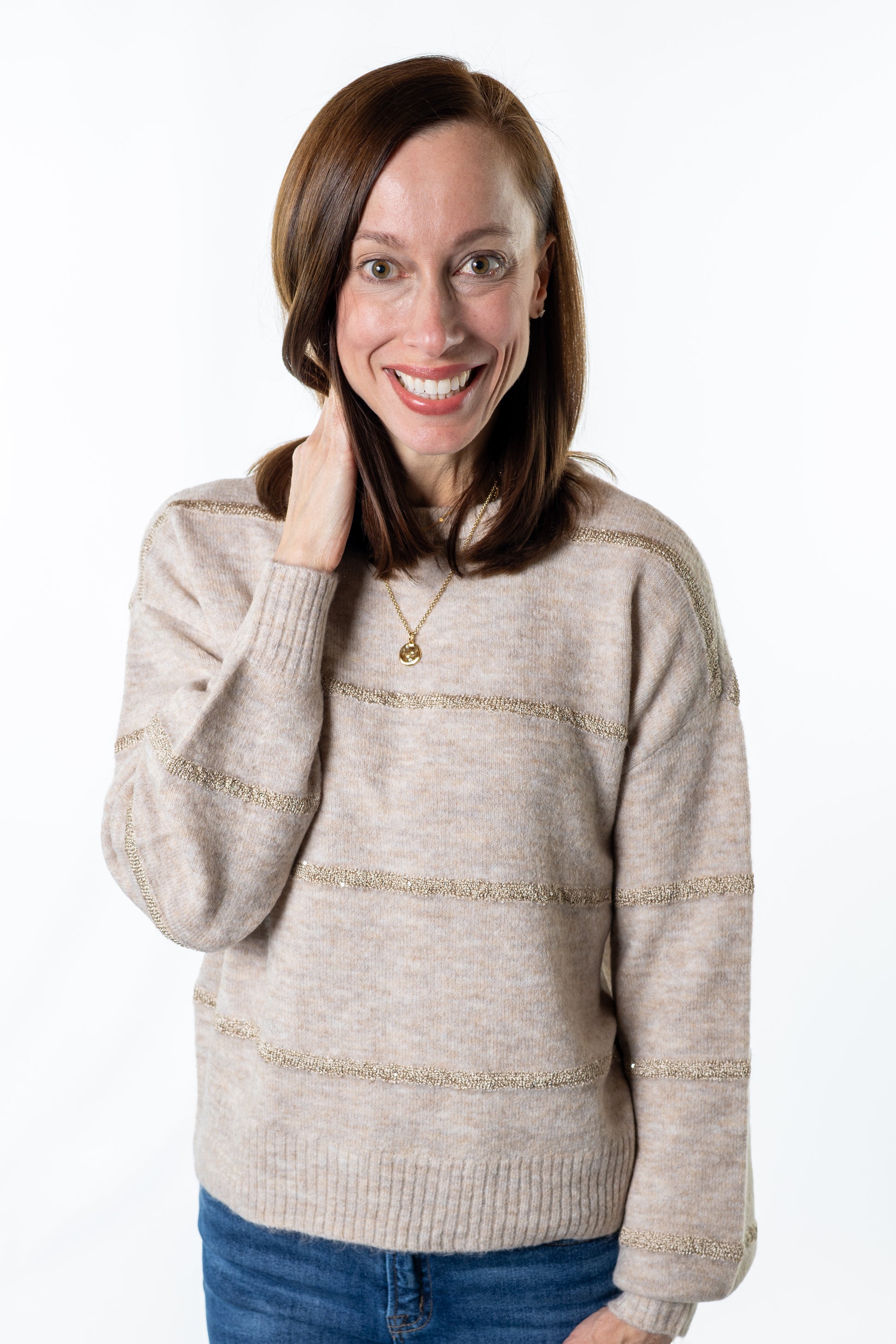 Woman wearing a beige sweater with gold accents on a white background holiday sweater
