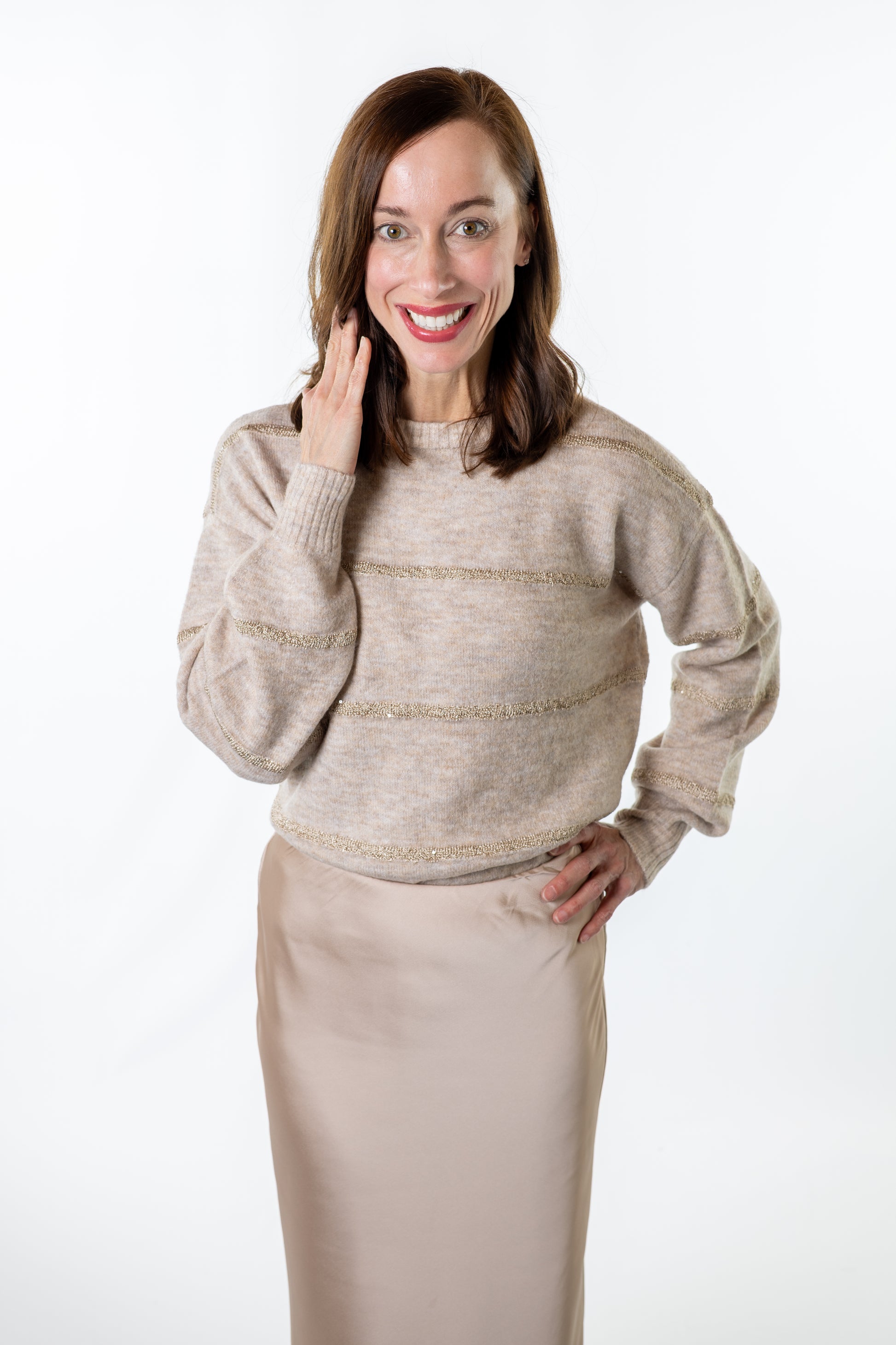 Woman wearing a beige sweater and netural beige skirt on a white background