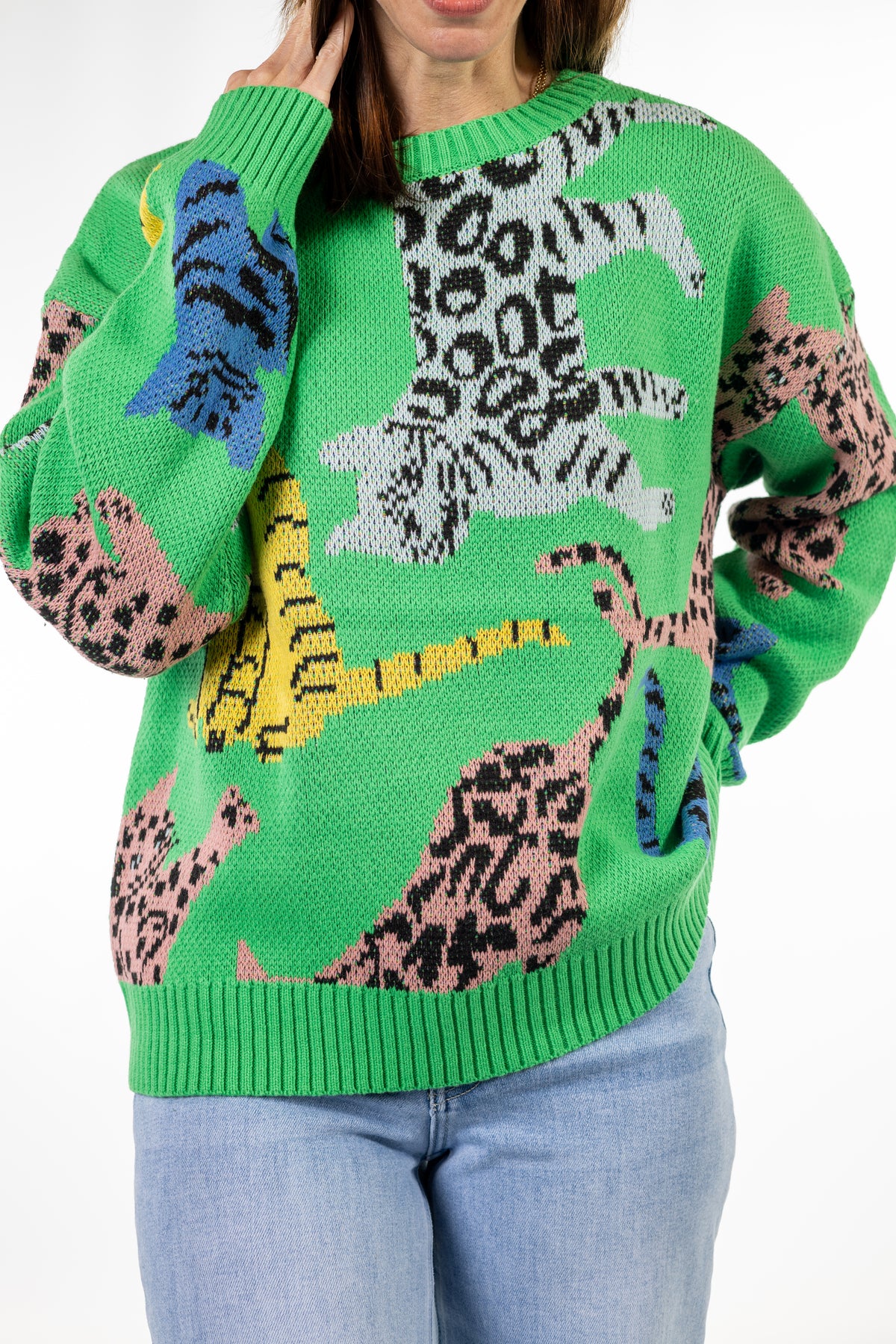 A bright green crewneck sweater featuring a colorful knit pattern of stylized animals in leopard, tiger, and zebra print, worn by a model with blue jeans.