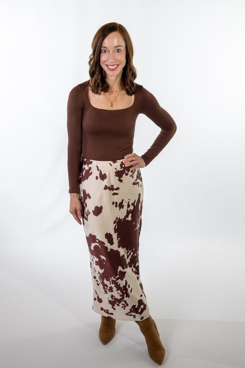 Woman wearing a brown top and cow abstract print skirt on a white background