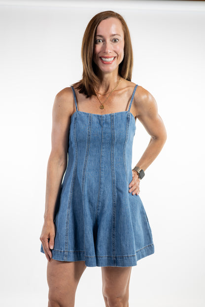 Woman wearing a blue denim romper with flared shorts, against a white background