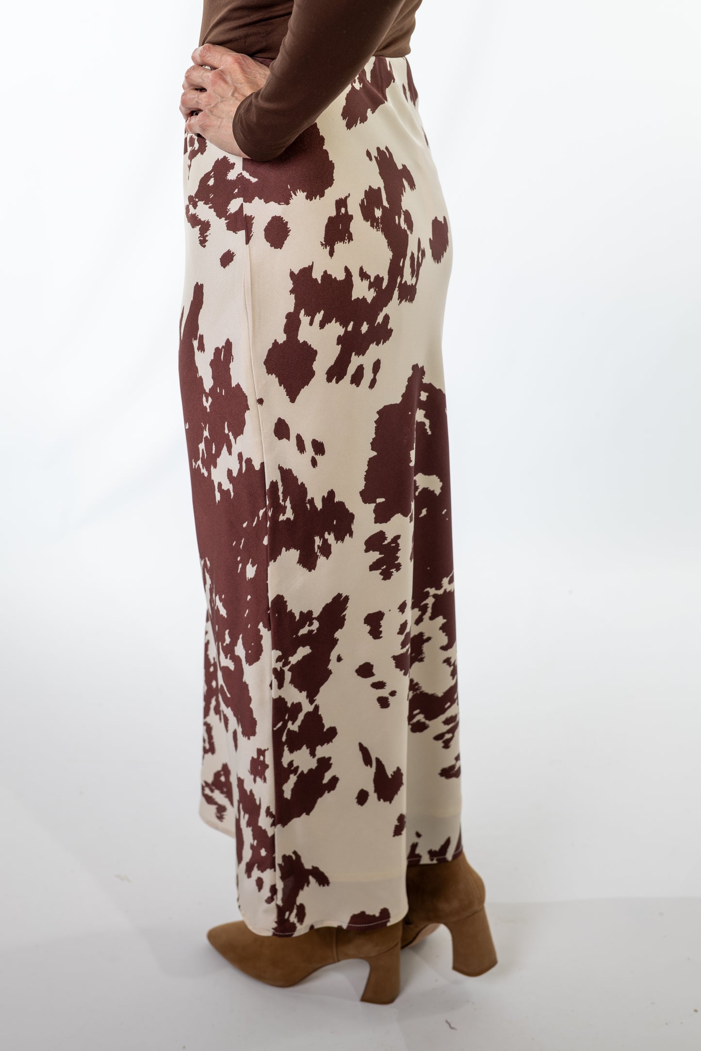 Person wearing a long, patterned skirt with brown and white colors on a plain background