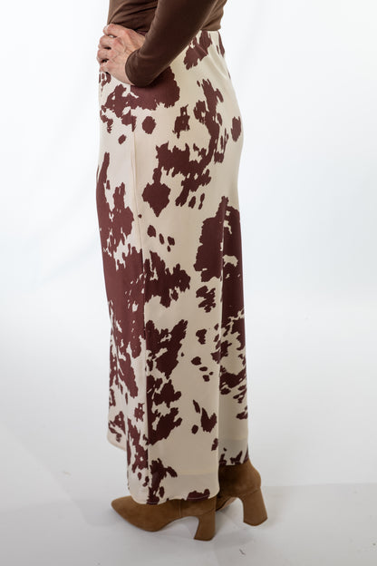 Person wearing a long, patterned skirt with brown and white colors on a plain background