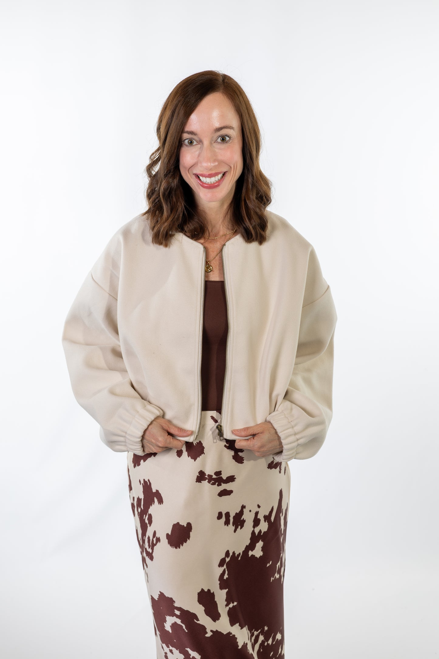 Woman wearing a beige jacket and cow print skirt on a white background