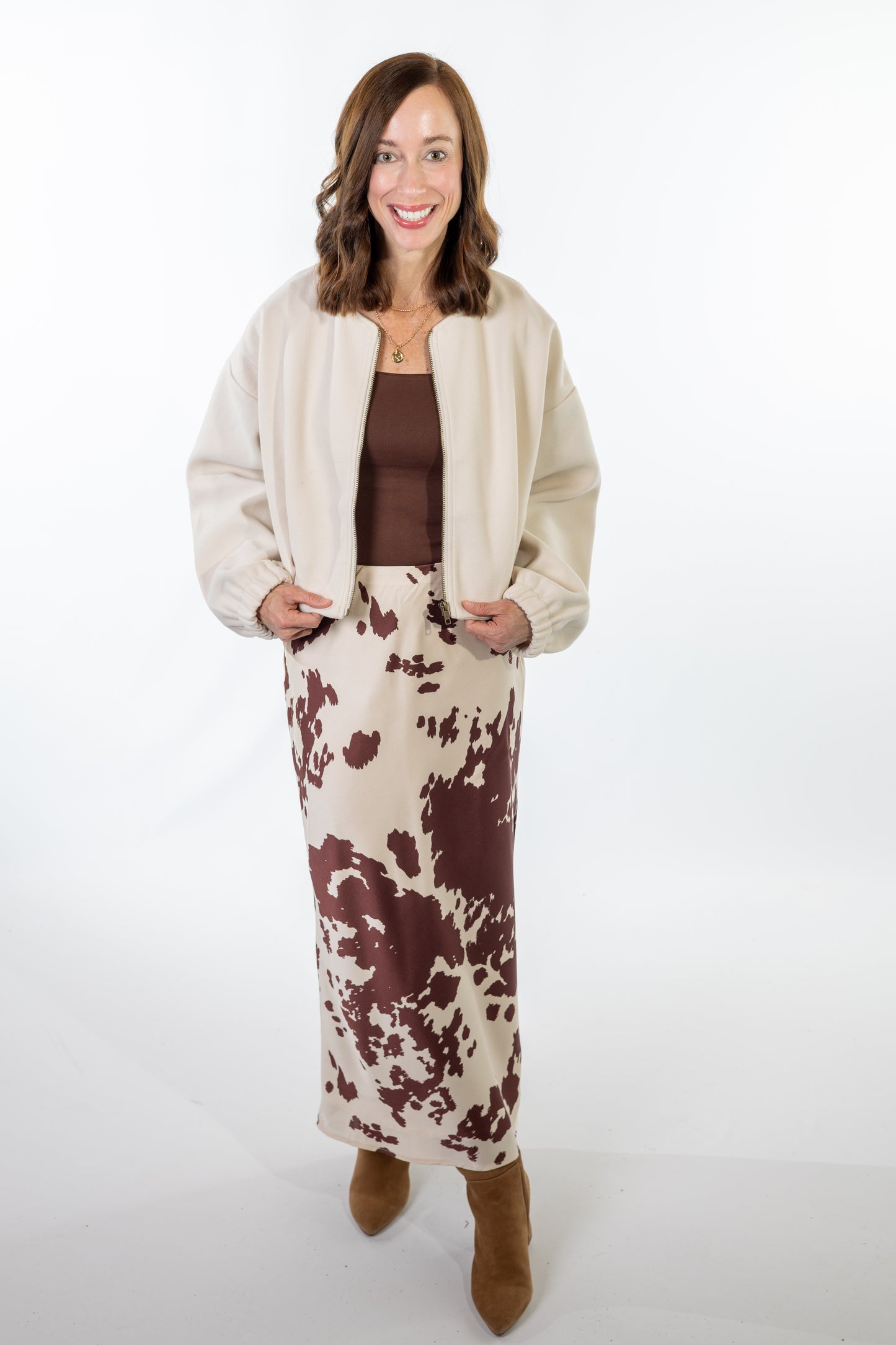 Woman wearing a cream jacket, brown top, and cow print skirt on a white background