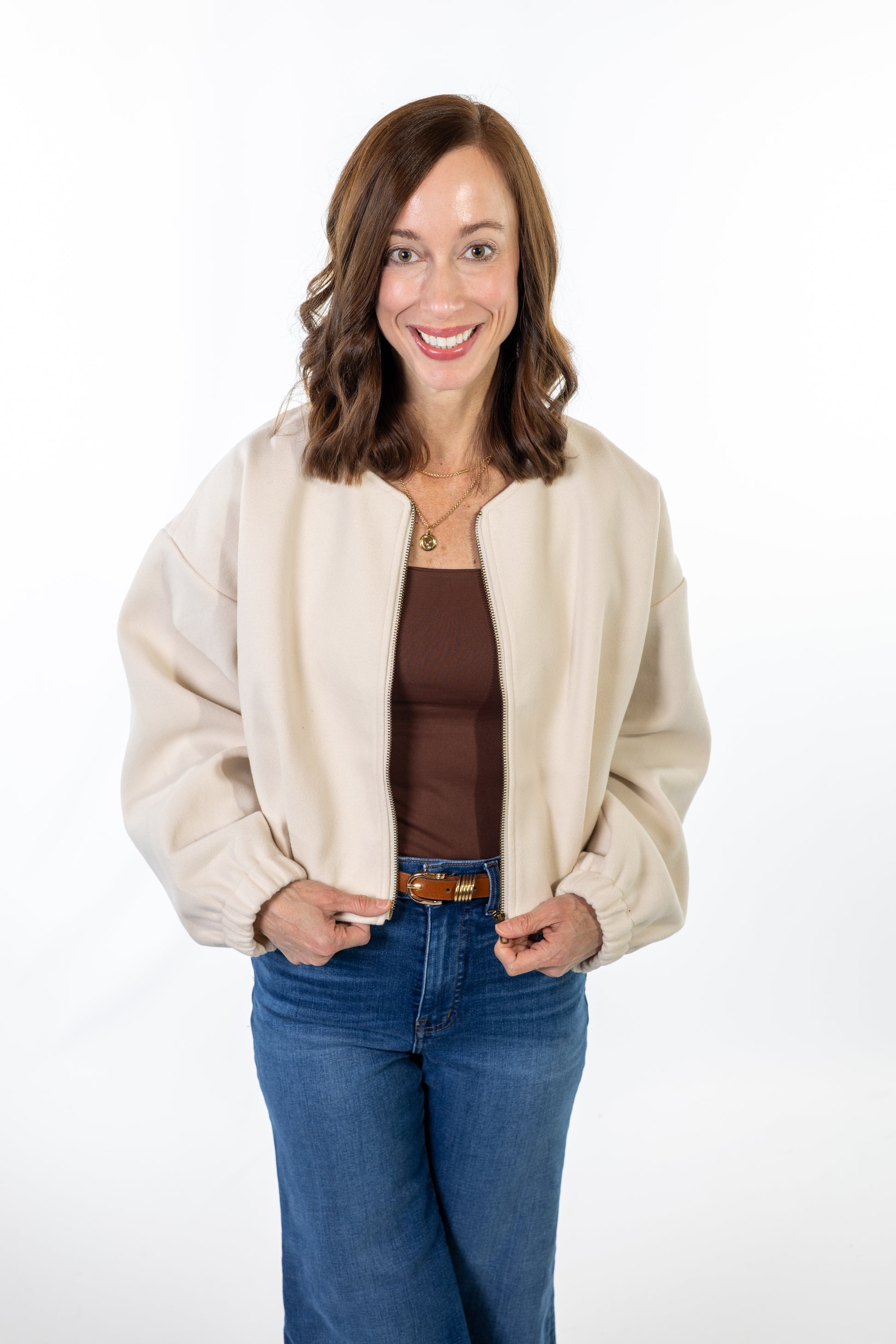 Woman wearing a beige cardigan over a brown top and blue jeans on a white background
