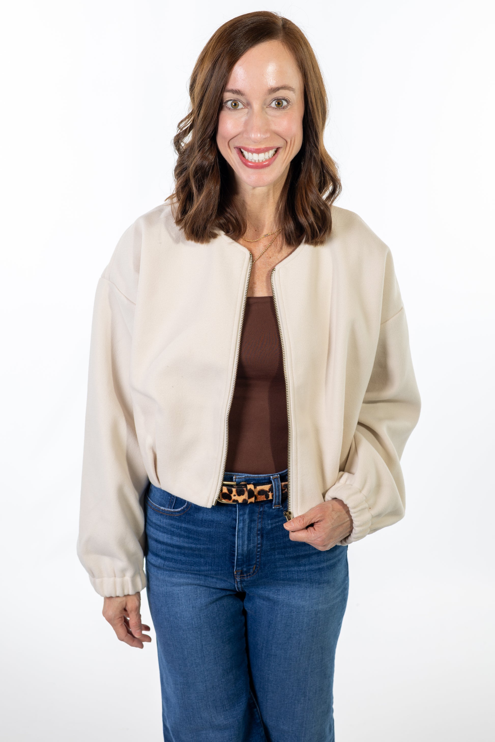 Woman wearing a cream jacket, brown top, and blue jeans on a white background