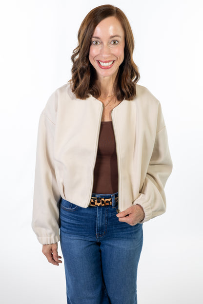 Woman wearing a cream jacket, brown top, and blue jeans on a white background