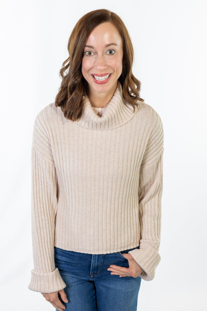 Woman wearing a beige turtleneck sweater and blue jeans on a white background