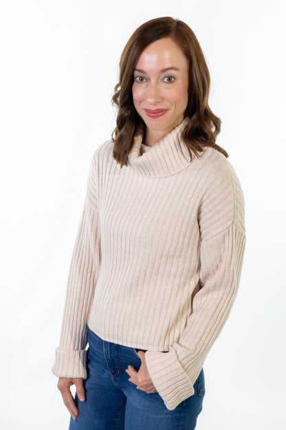 Woman wearing a beige ribbed sweater and blue jeans on a white background