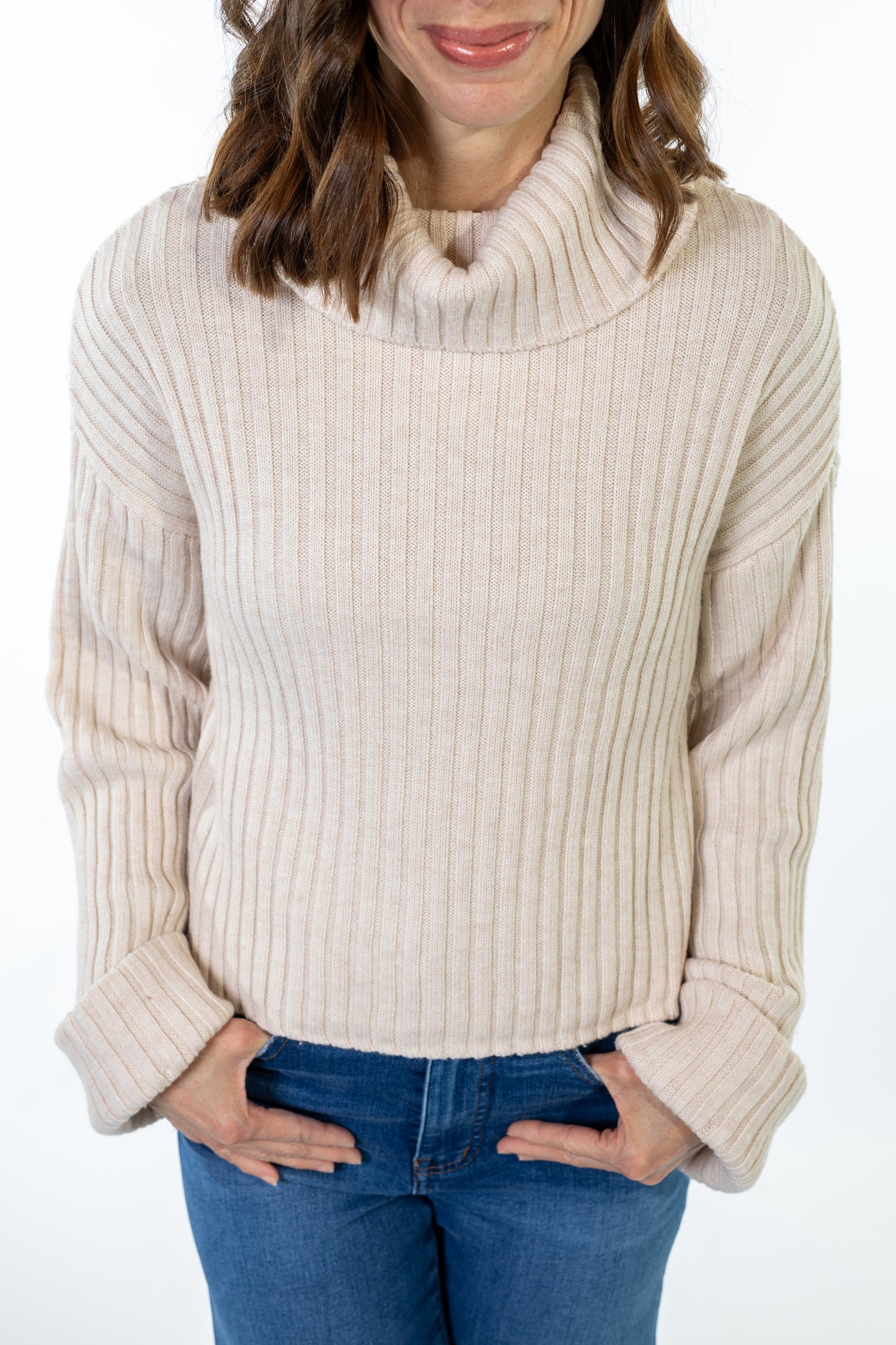 Woman wearing a beige ribbed sweater and blue jeans on a white background