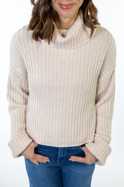 Woman wearing a beige ribbed sweater and blue jeans on a white background