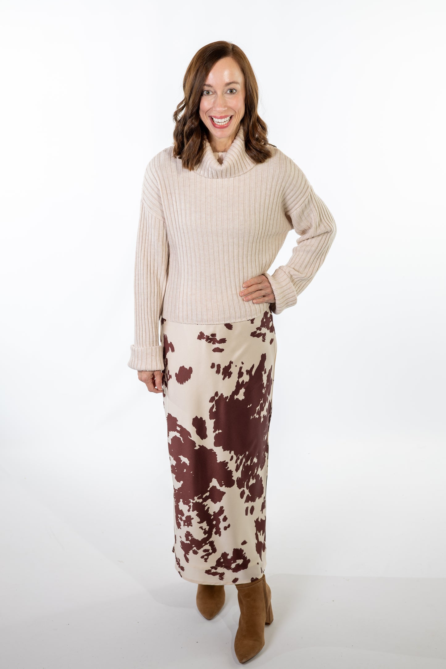 Woman wearing a beige oatmeal sweater and cow animal print skirt on a white background
