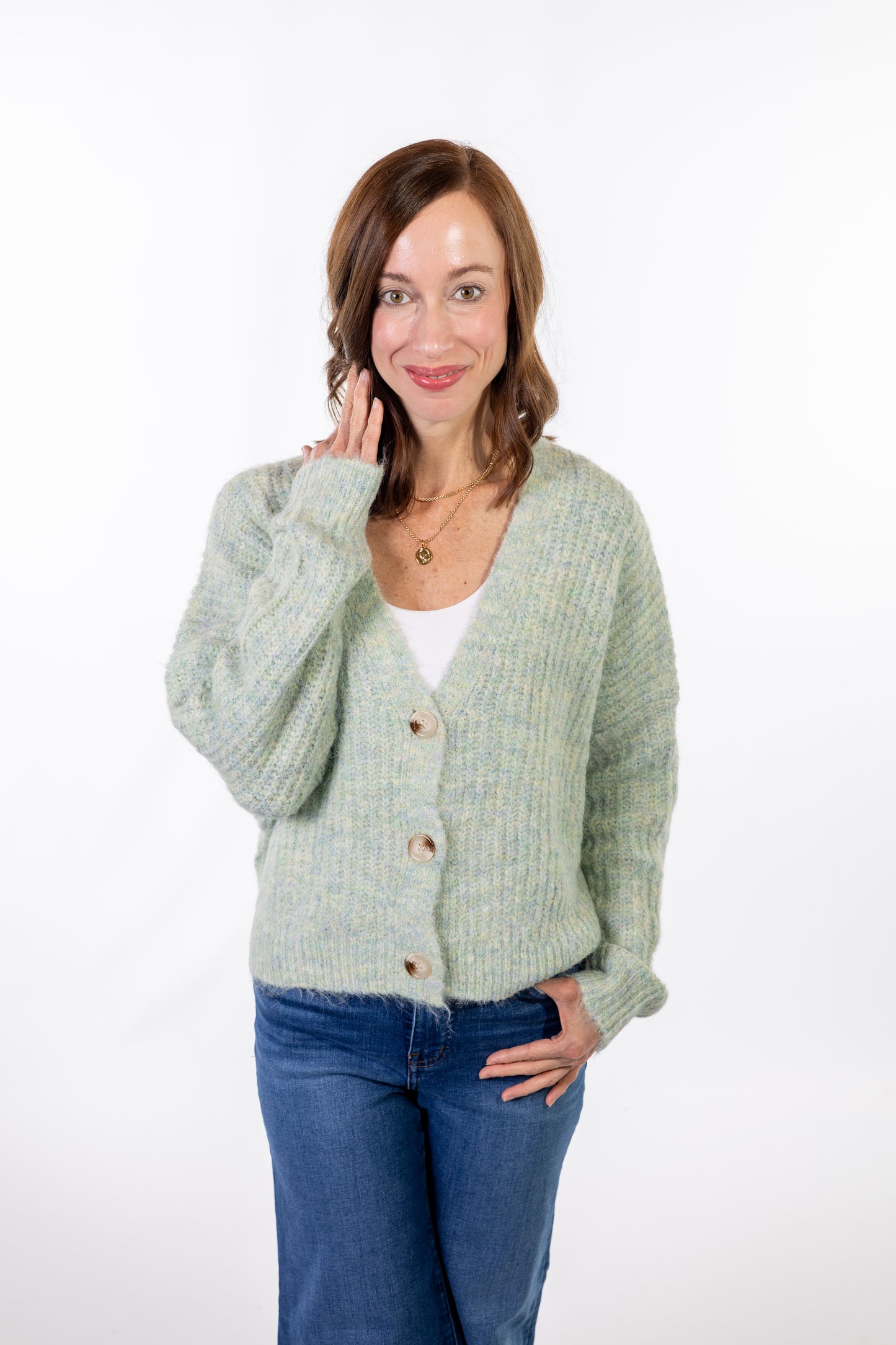 Woman wearing a light green cardigan over a white shirt and blue jeans on a white background