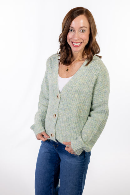 Woman wearing a mint green cardigan over a white shirt and blue jeans on a white background
