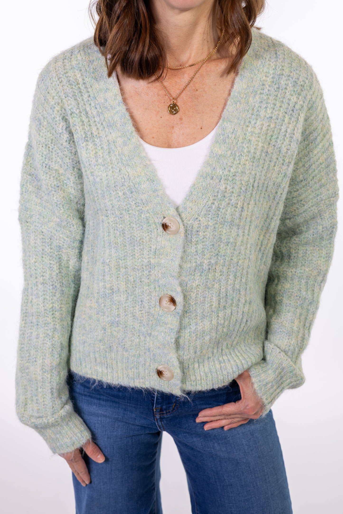 Person wearing a light mint green cardigan over a white shirt with blue jeans on a white background