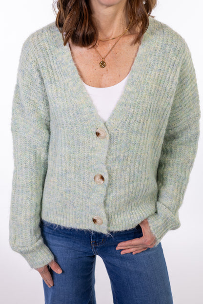 Person wearing a light mint green cardigan over a white shirt with blue jeans on a white background