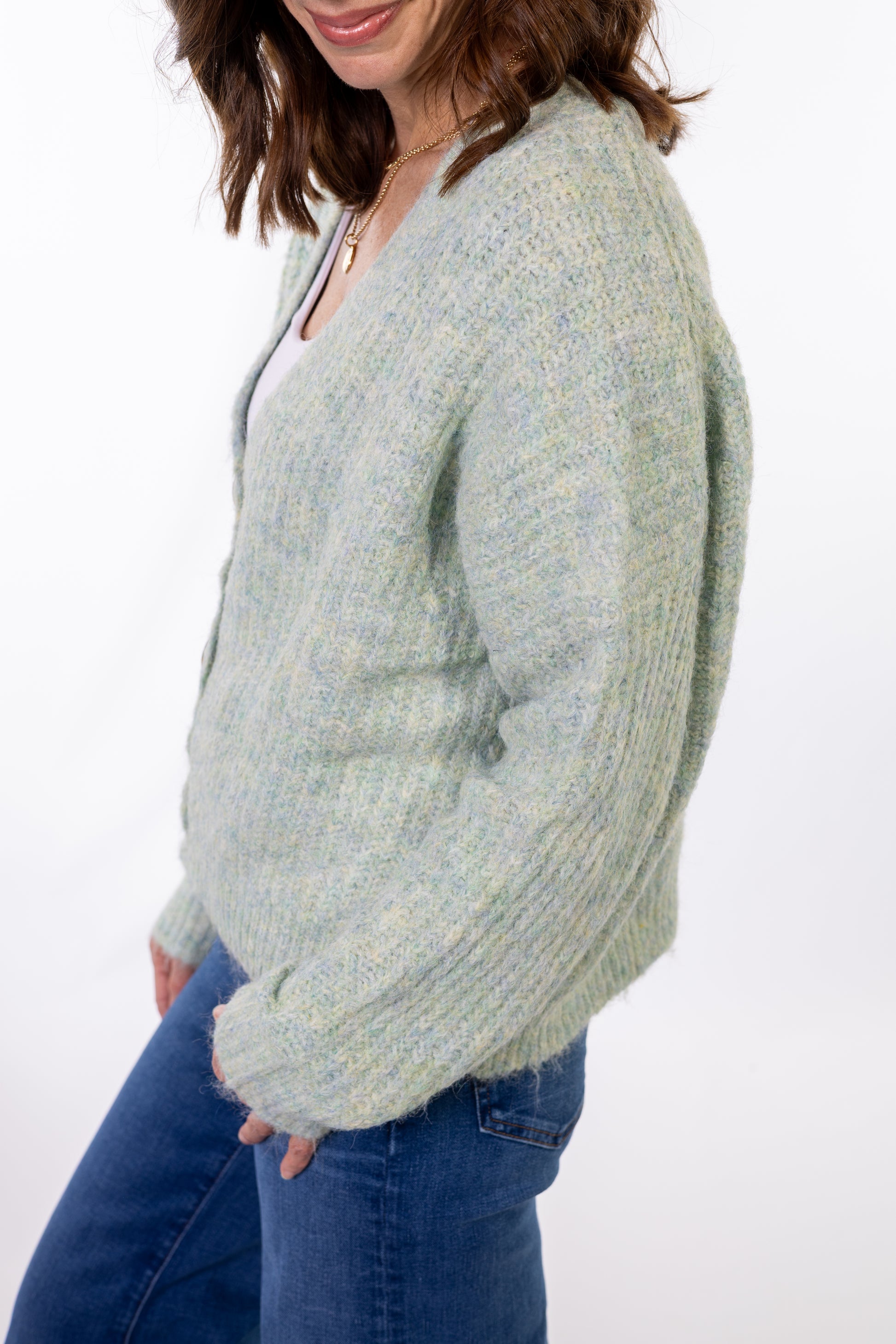 Woman wearing a light green sweater and blue jeans on a white background