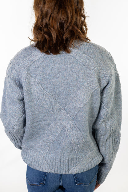 Person wearing a gray cable knit sweater on a white background