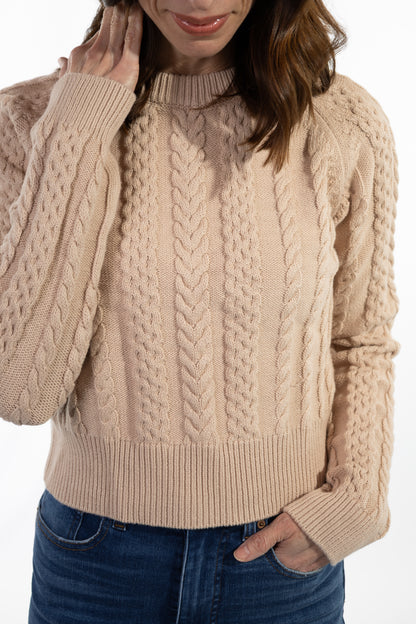 Person wearing a beige cable knit sweater with blue jeans on a white background