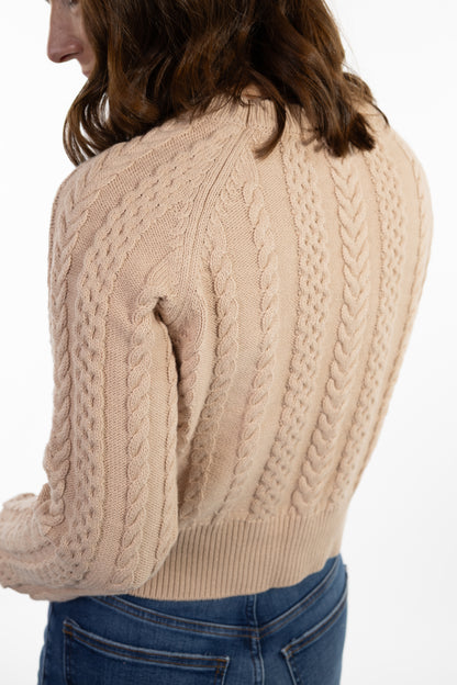 Beige cable knit sweater worn by a person on a white background