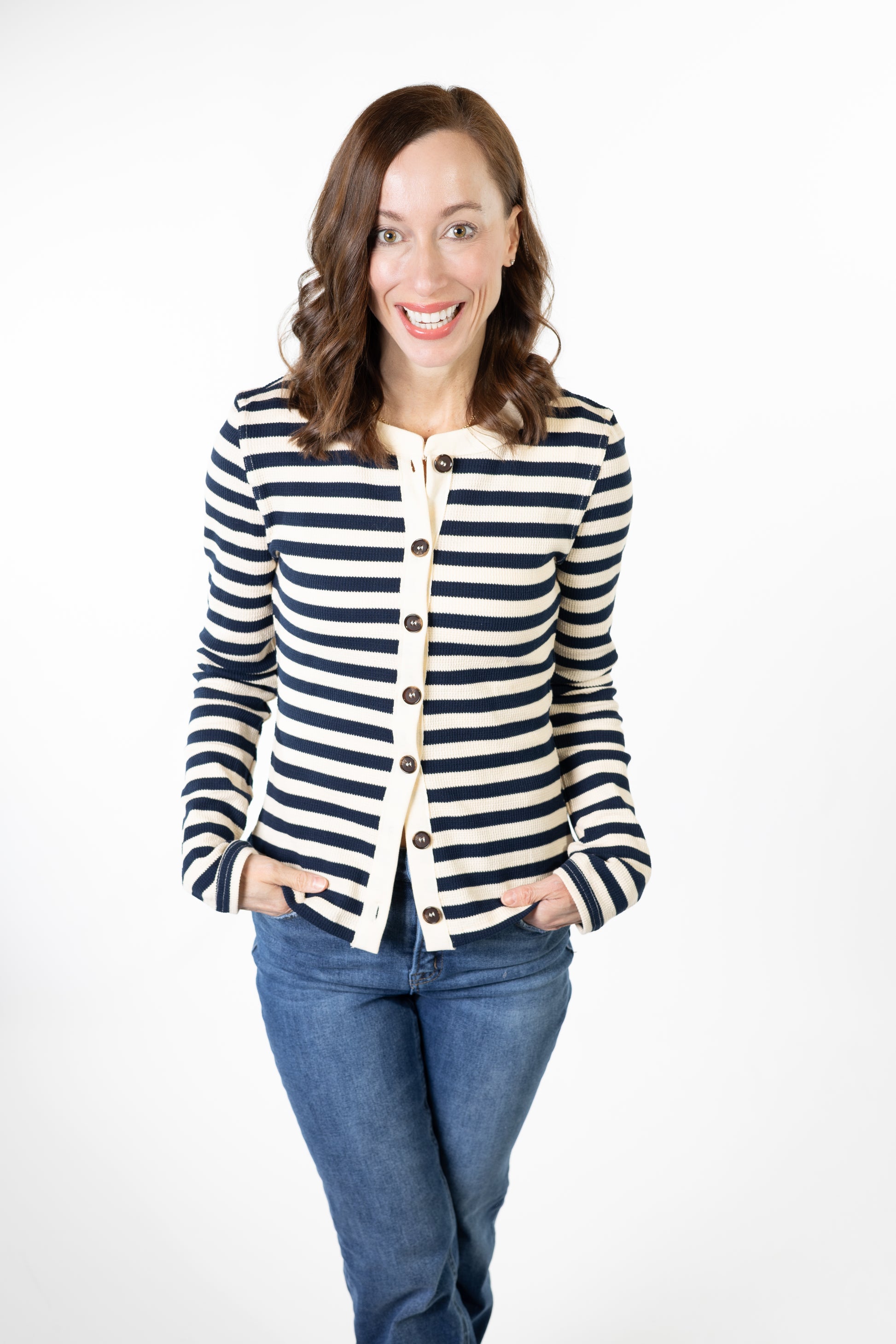 Woman wearing a striped navy and cream cardigan and jeans on a white background